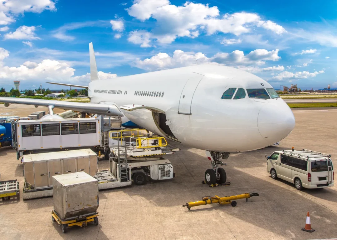 A white cargo plane being loaded with freight containers on an airport tarmac under a blue sky.