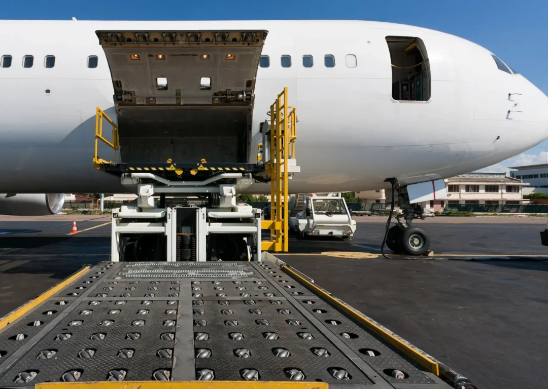 A white cargo aircraft on an airport tarmac with its door open and loading platform extended.