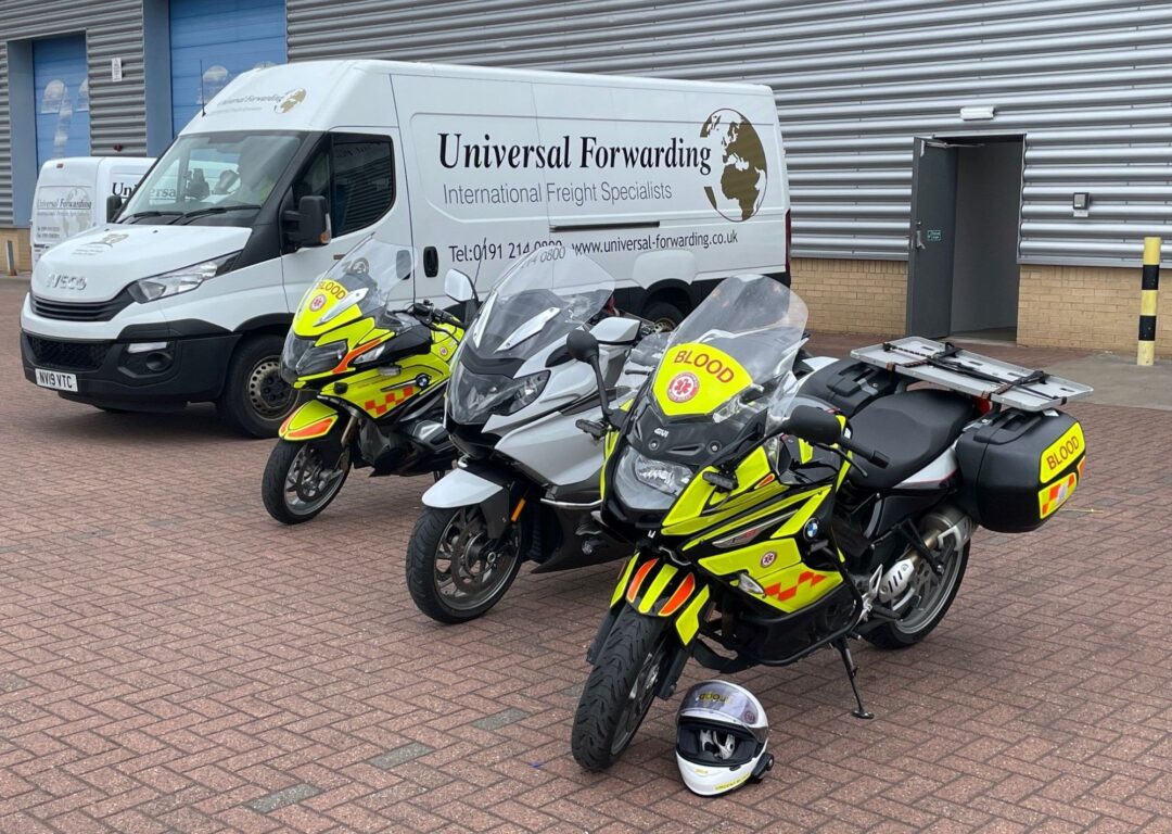 Three high-visibility blood bikes parked in a row next to a Universal Forwarding van.