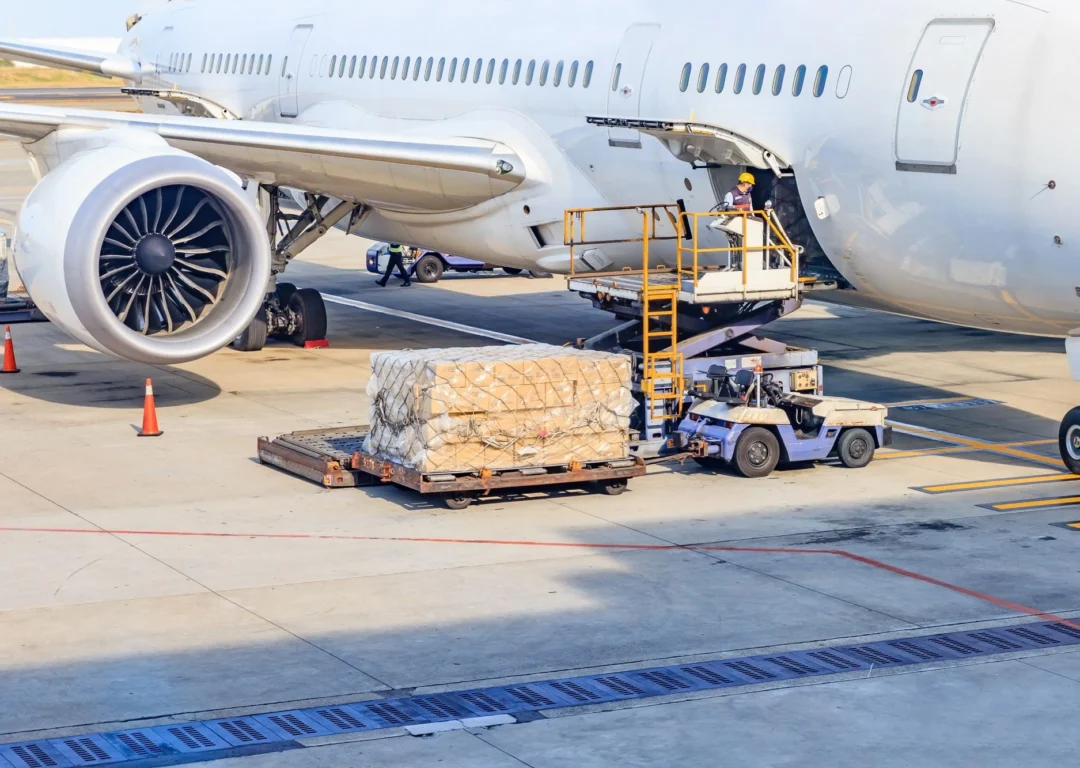 A cargo loader being used to move a large, netted pallet of goods into a white airplane.