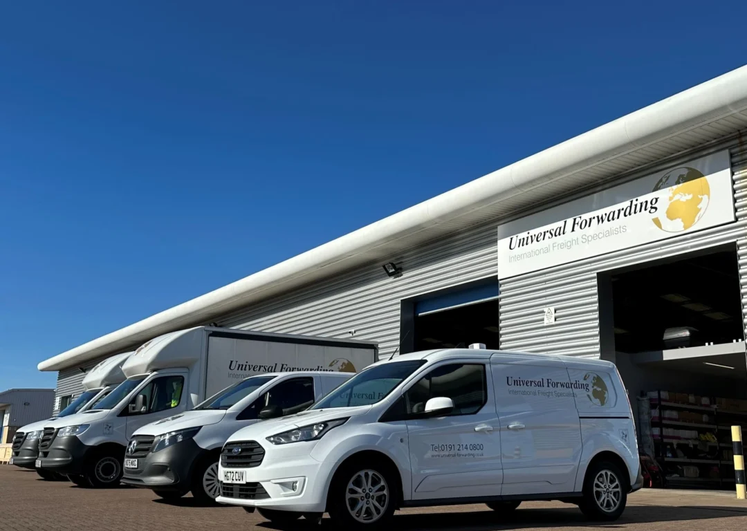A fleet of white Universal Forwarding vans and trucks parked in front of a modern warehouse under a clear blue sky.