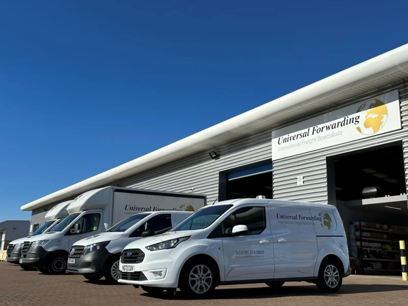 A fleet of white Universal Forwarding vans and trucks parked in front of a modern warehouse under a clear blue sky.