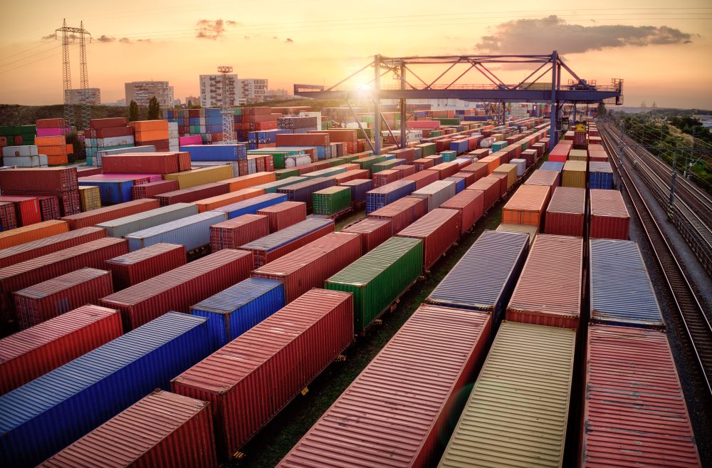 Rows of dozens of freight containers, in colours red, blue, yellow, green, and orange, lined up alongside and on rail tracks. 